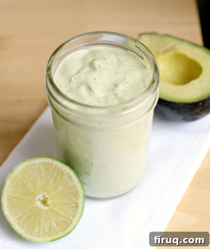 Creamy Avocado Tortellini Salad 5 A mason jar filled with bright green avocado herb dressing, flanked by a fresh lime and a halved avocado, highlighting the key ingredients for the creamy dressing