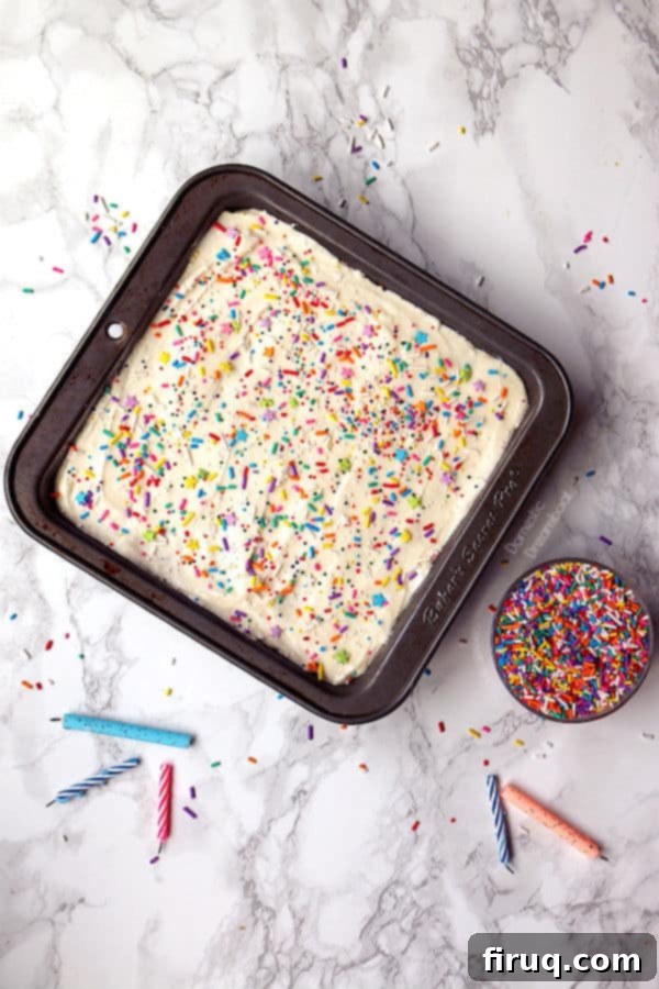 Easy Sprinkle Cake Slice A slice of easy sprinkle cake with colorful jimmie sprinkles and creamy frosting on a white plate. The cake shows a soft, moist vanilla crumb.