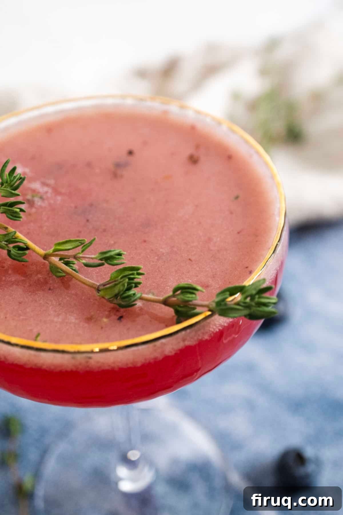Blueberry Smash Mocktail 2 A vibrant blueberry mocktail garnished with a sprig of fresh thyme, served in an elegant glass, ready to be enjoyed.
