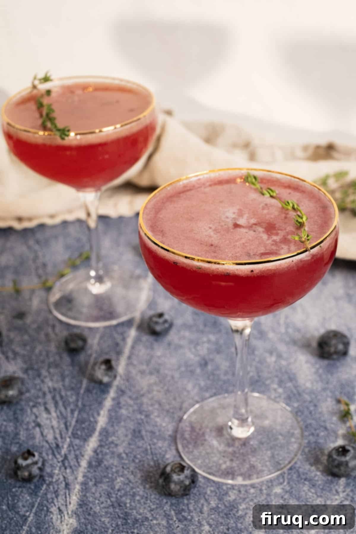 Blueberry Smash Mocktail 4 Two perfectly prepared blueberry mocktails, each garnished with a sprig of fresh thyme, presented in elegant glasses for serving.