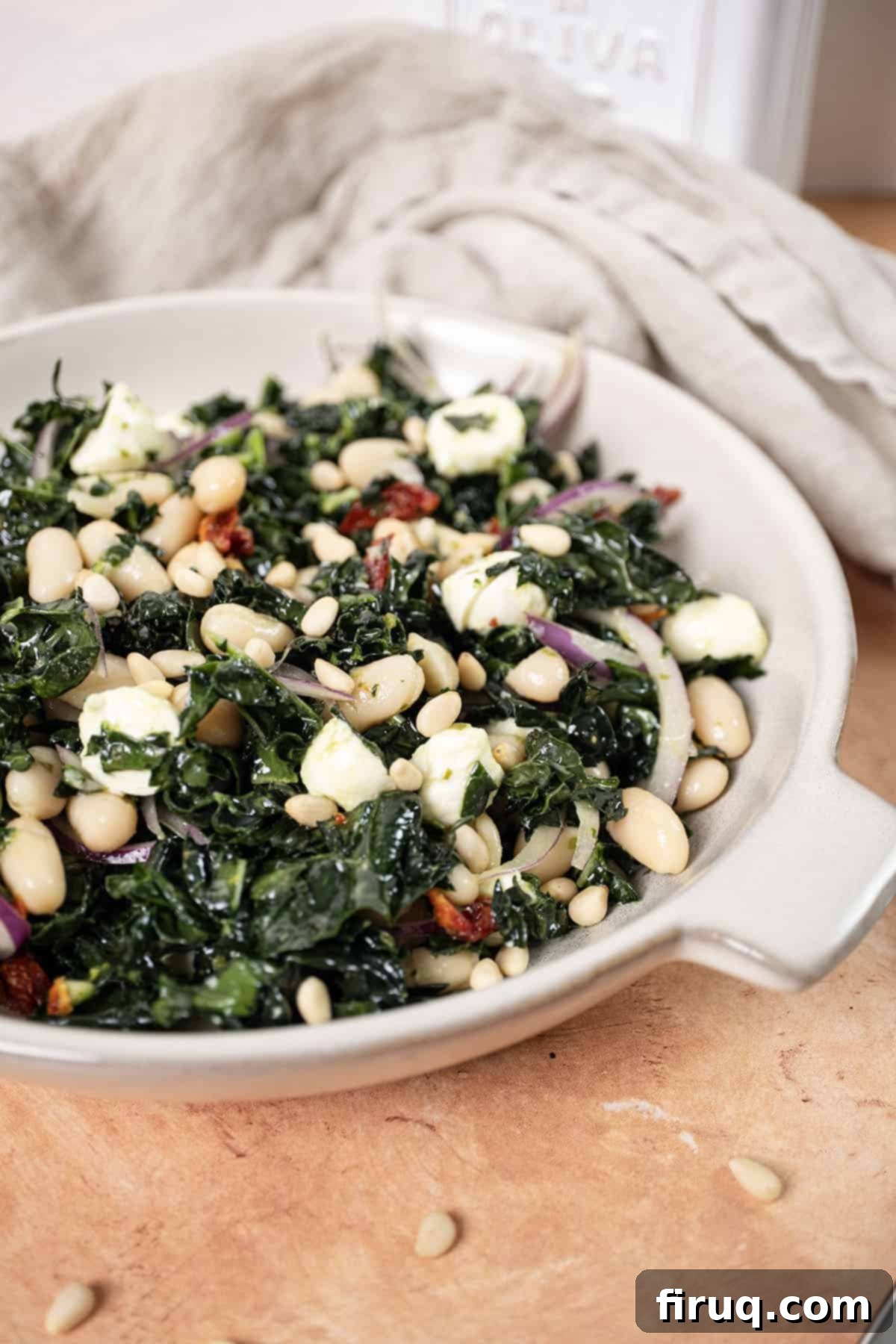 Hearty Kale and White Bean Salad 2 A beautifully presented Kale and Cannellini Bean salad in a large bowl, garnished with toasted pine nuts. The vibrant green of the kale contrasts with the white beans and red sundried tomatoes.