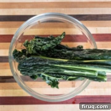 Hearty Kale and White Bean Salad 4 Close-up of hands massaging lacinato kale leaves with olive oil in a bowl, showing the leaves softening.