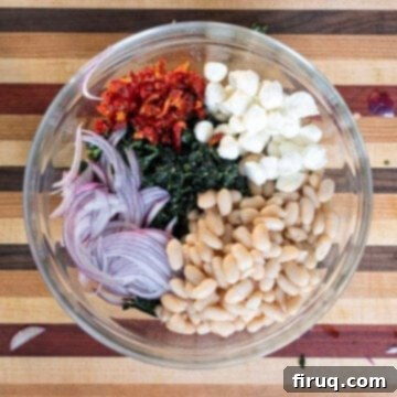 Hearty Kale and White Bean Salad 6 A large bowl containing chopped kale, drained cannellini beans, mozzarella pearls, sundried tomatoes, and thinly sliced red onion before dressing.