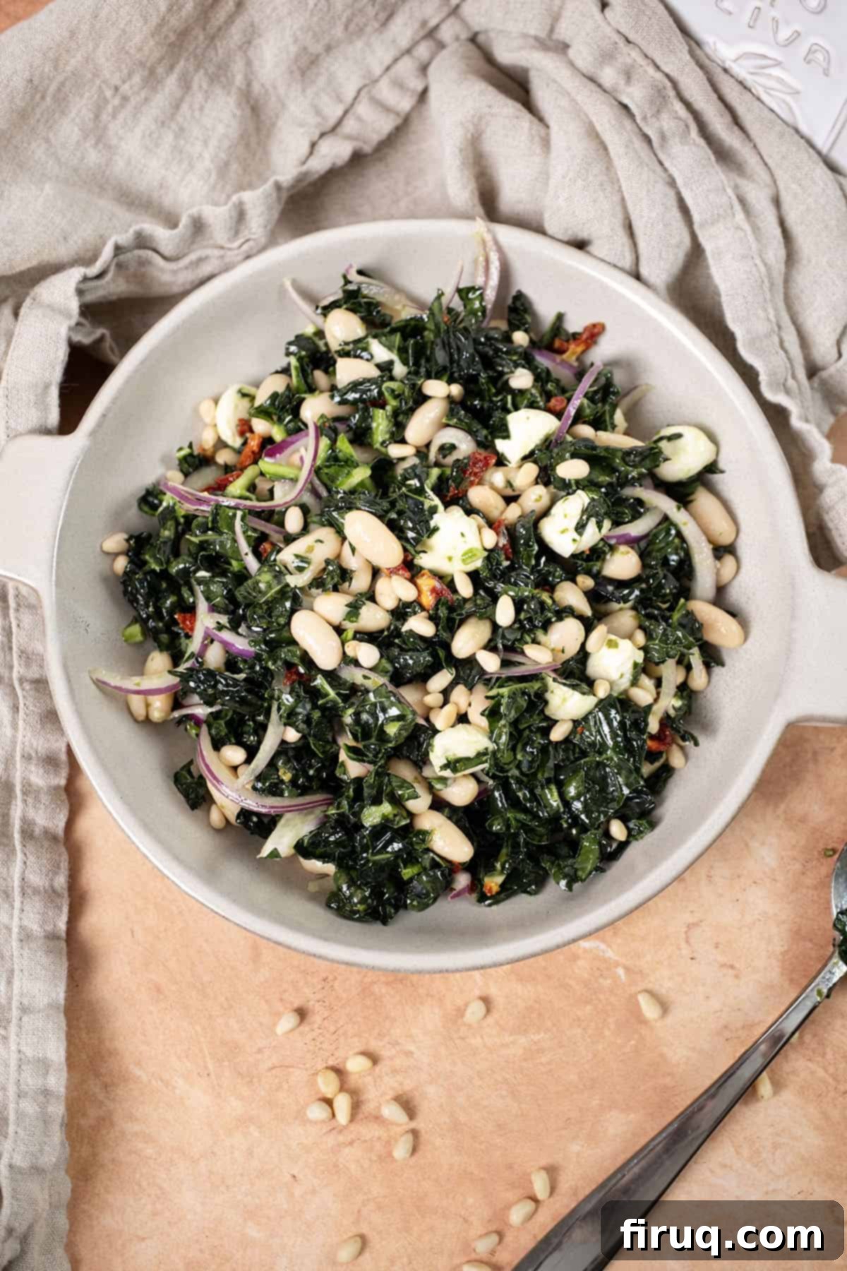 Hearty Kale and White Bean Salad 8 A vibrant Kale and Cannellini Bean salad in a large serving bowl, topped with a generous sprinkle of golden pine nuts, ready to be served.