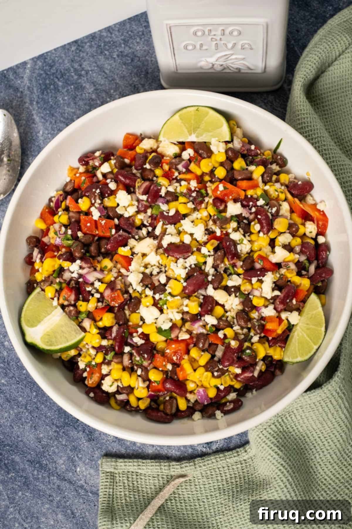 Tex-Mex Treasure Salad 2 A large, inviting bowl of colorful Cowboy Caviar Salad, beautifully garnished with fresh lime wedges, showcasing the vibrant black beans, kidney beans, sweet corn, crisp red peppers, and aromatic cilantro, all coated in a creamy dressing.