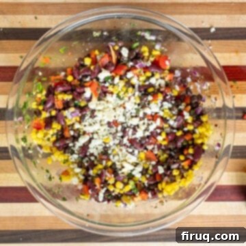 Tex-Mex Treasure Salad 5 The savory dressing and crumbled cotija cheese are being meticulously stirred into the vibrant mixture of beans and fresh vegetables in a large bowl, creating a creamy and well-coated salad.