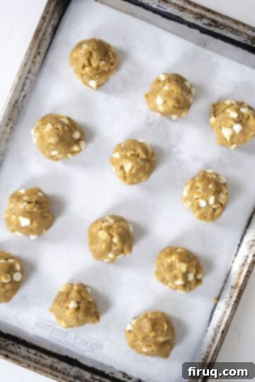 Irresistible Chewy White Chocolate Macadamia Nut Cookies 9 Cookies rolled into balls on a parchment paper lined baking sheet.