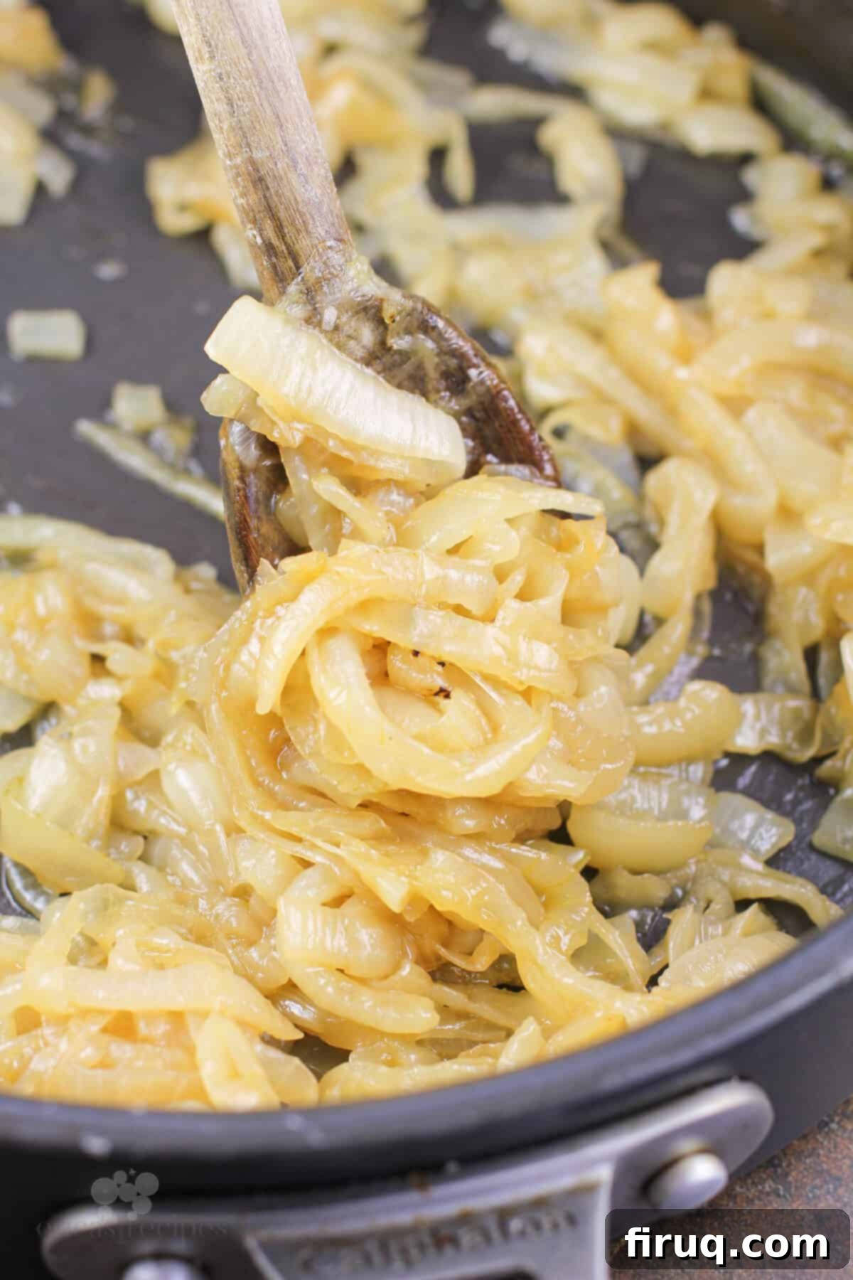 Sticky Honey Bourbon Onions 3 Cooked onions in a skillet with a wooden spoon, showing their softened and lightly browned texture.