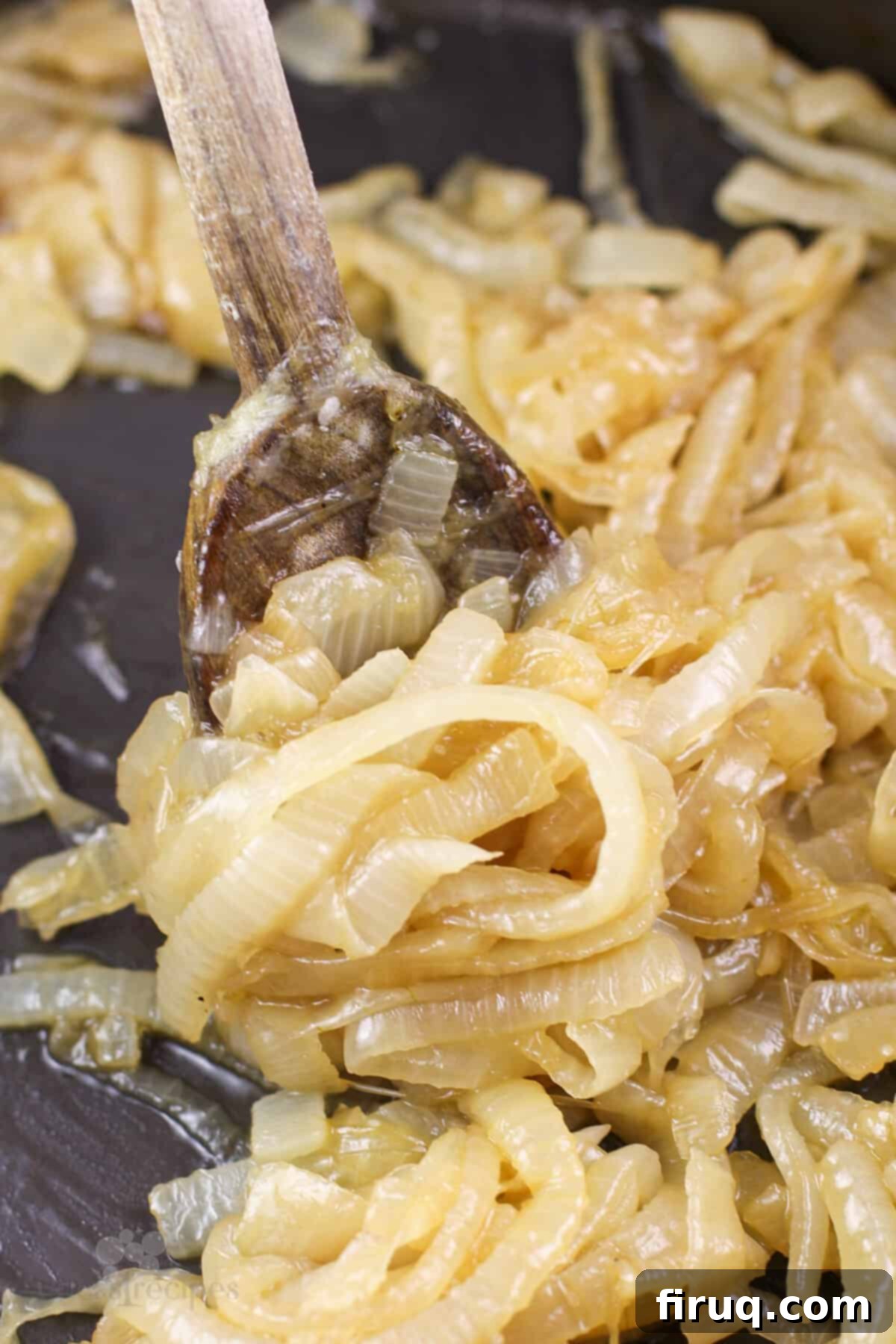 Sticky Honey Bourbon Onions 8 Prepared honey bourbon caramelized onions in a skillet with a wooden spoon, ready to be served.