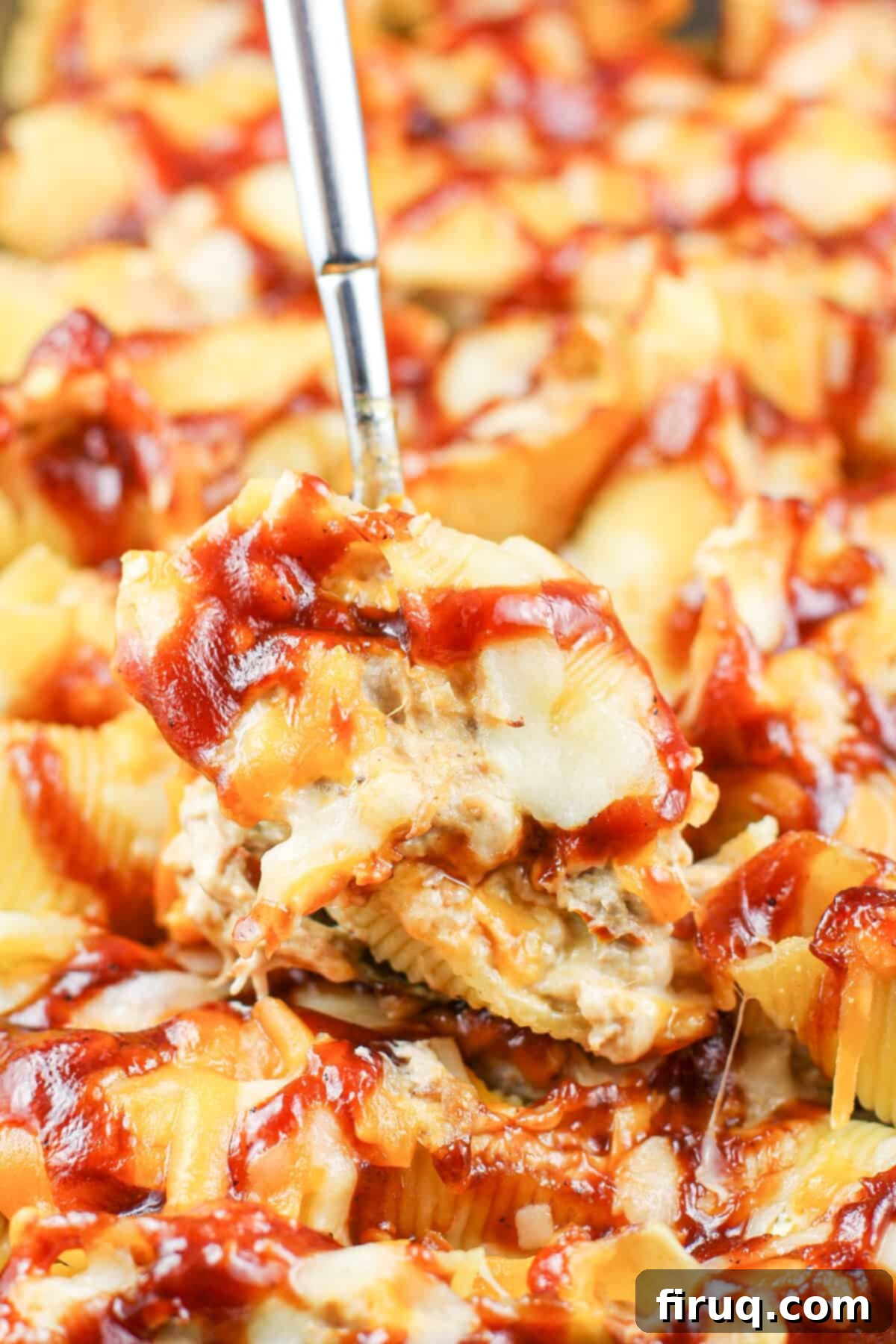 Cheesy BBQ Pulled Pork Stuffed Shells 2 A spoon lifting a perfectly baked, cheesy BBQ pulled pork stuffed pasta shell, showcasing the delicious filling and golden top.