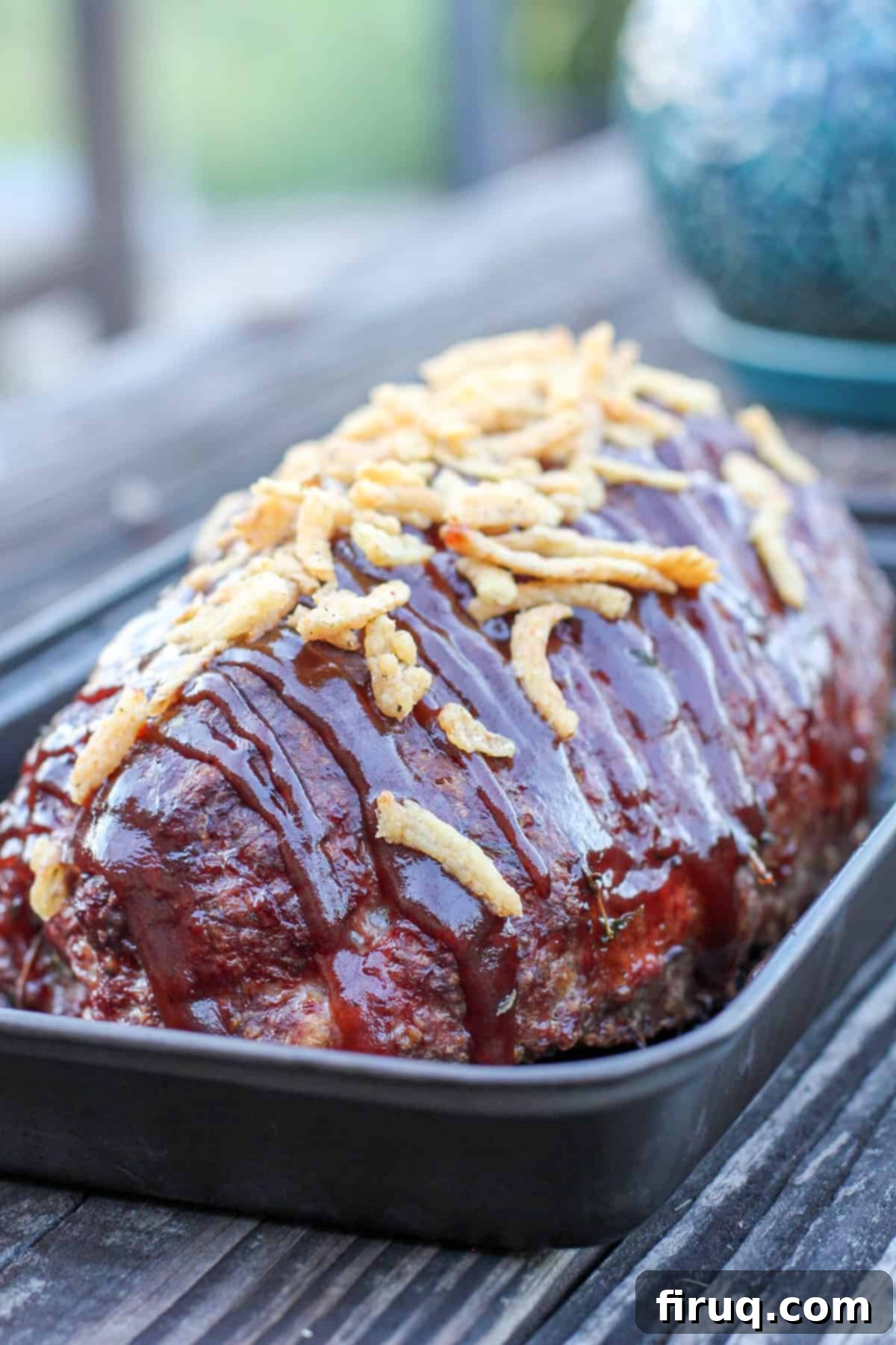 Signature Smoked Meatloaf 3 Prepared smoked meatloaf resting in a grill-proof pan on a rustic wooden table, showcasing its rich color and tender texture.