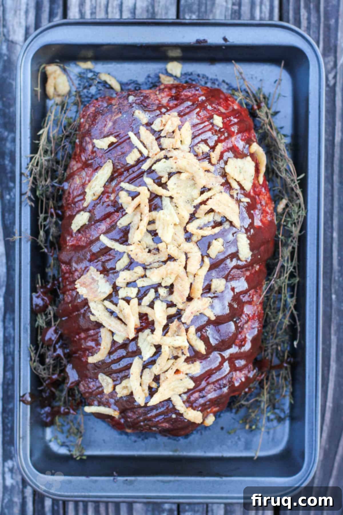 Signature Smoked Meatloaf 6 Close-up top-down shot of the finished smoked meatloaf, generously topped with BBQ sauce and crispy fried onions, ready for slicing.