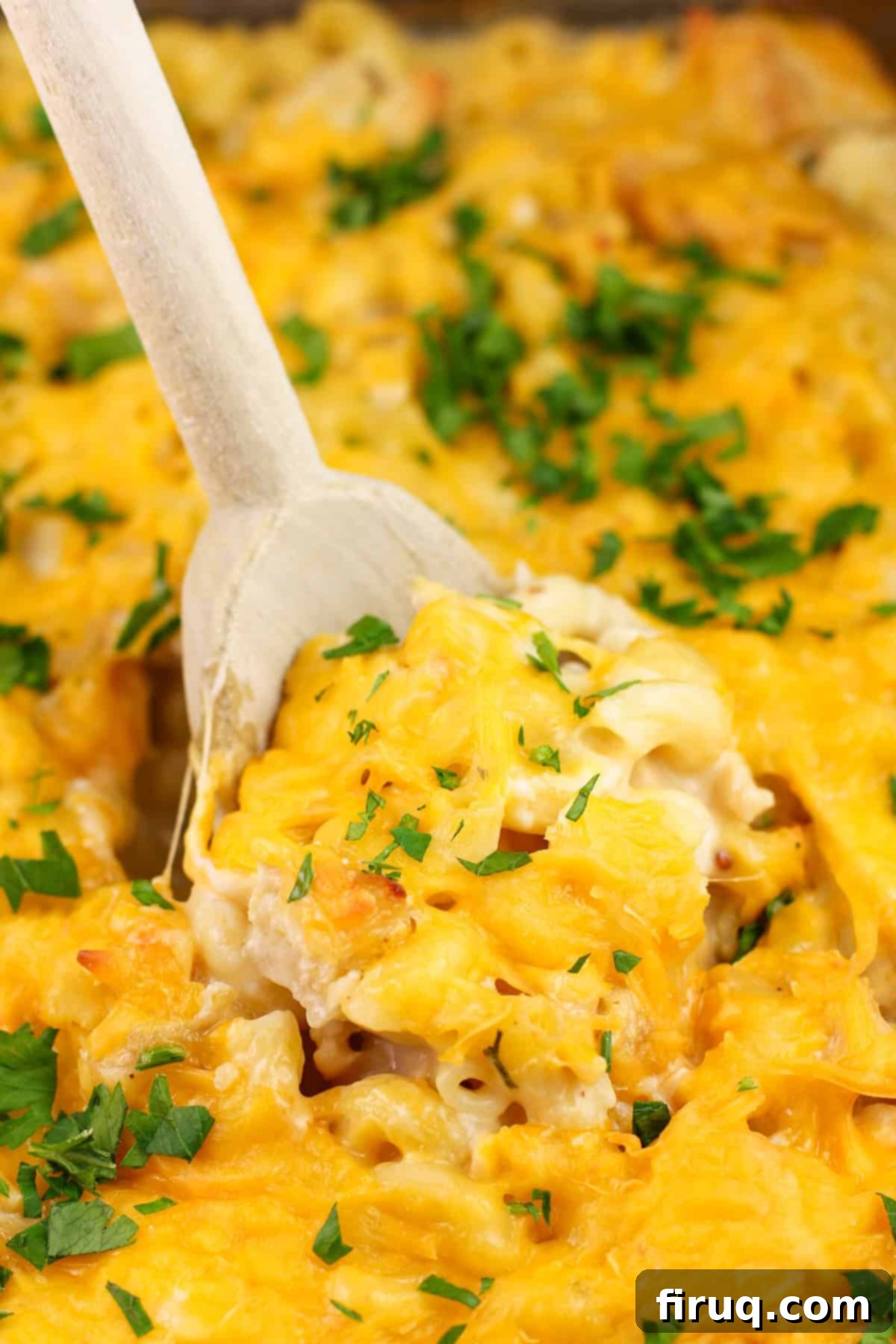Ultimate Cheesy Chicken Macaroni Casserole 2 A wooden spoon being inserted into a freshly cooked cheesy chicken macaroni casserole, showing its golden-brown top and bubbling cheese.