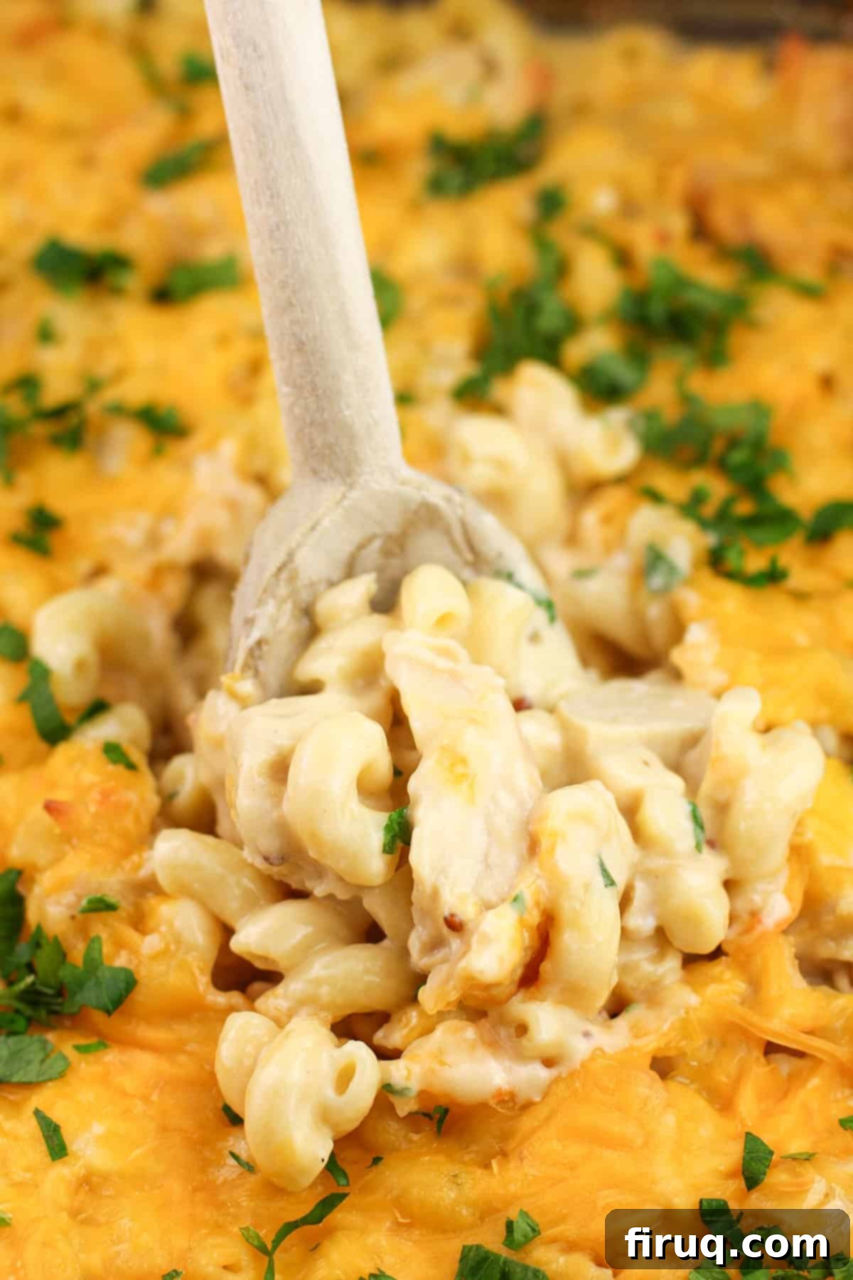 Ultimate Cheesy Chicken Macaroni Casserole 5 A wooden spoon being inserted into a freshly cooked cheesy chicken macaroni casserole, showing its golden-brown top and bubbling cheese.