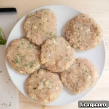 Gourmet Gorgonzola Grilled Chicken Burger 5 Four perfectly formed, round ground chicken patties resting on a plate, lightly seasoned with salt and pepper.