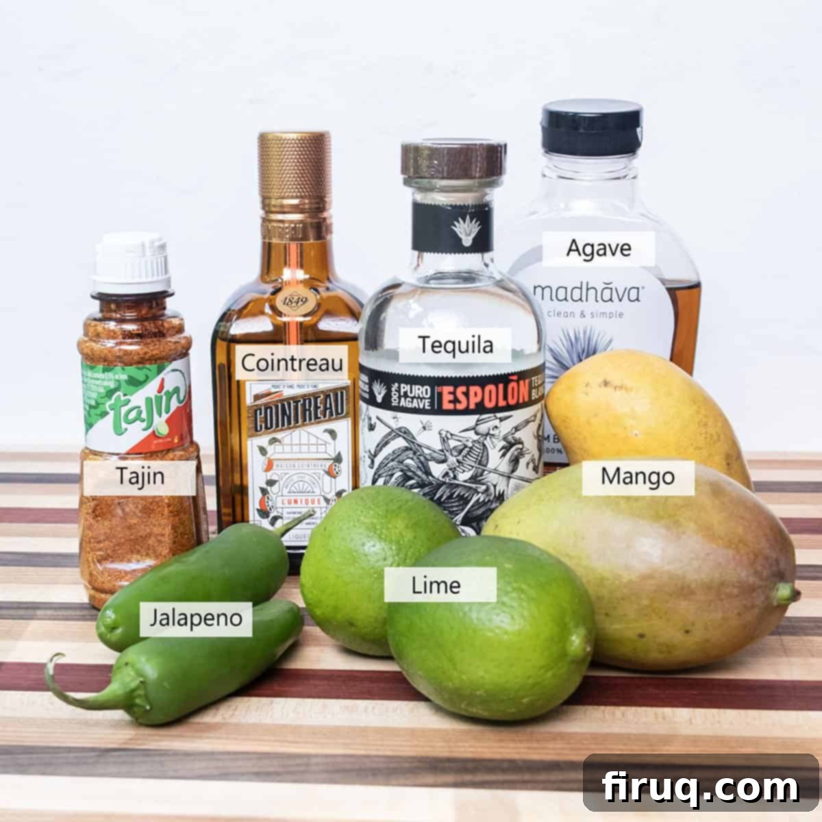 Blazing Mango Margarita 3 A collection of fresh ingredients laid out on a wooden board, including a sliced mango, limes, jalapenos, a bottle of tequila, and Cointreau, ready for making a spicy mango margarita.