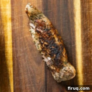 Rustic Italian Cast Iron Pork Tenderloin 7 Cooked pork tenderloin resting on a cutting board, ready to be sliced.