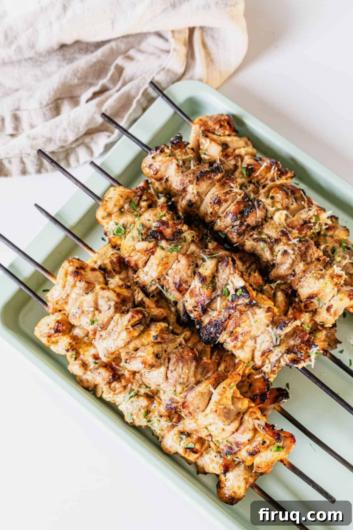 Irresistible Garlic Parmesan Chicken Skewers 2 Garlic parm chicken skewers on a baking pan basted with parm sauce.