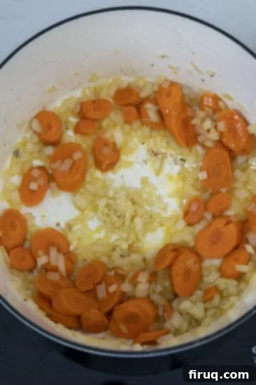 Creamy Tuscan Sausage and Potato Soup 6 Carrots, onions, and minced garlic sautéing in a pan.