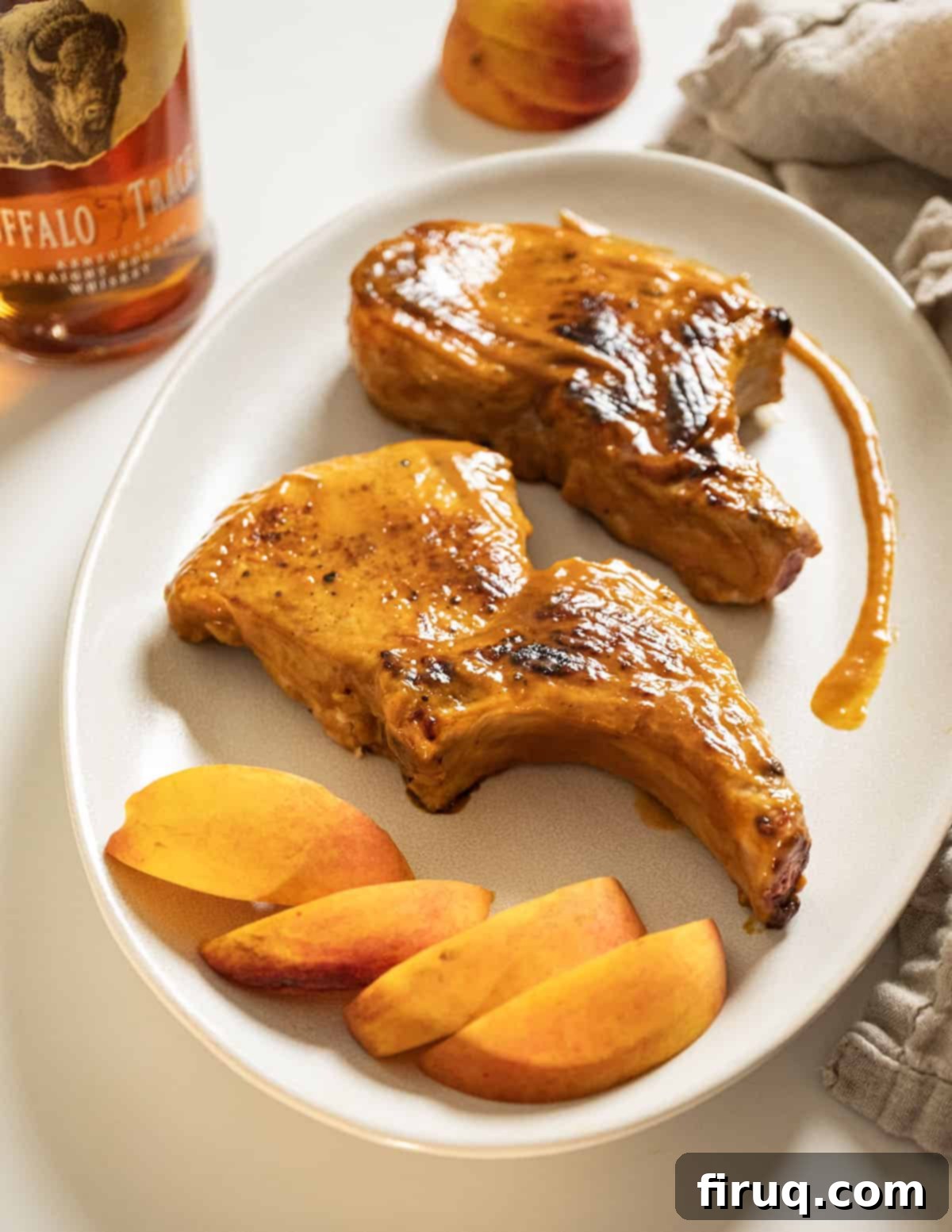 Pork Chops with Bourbon Peach Glaze 2 Bourbon peach glazed pork chops on a plate garnished with peaches and extra sauce.