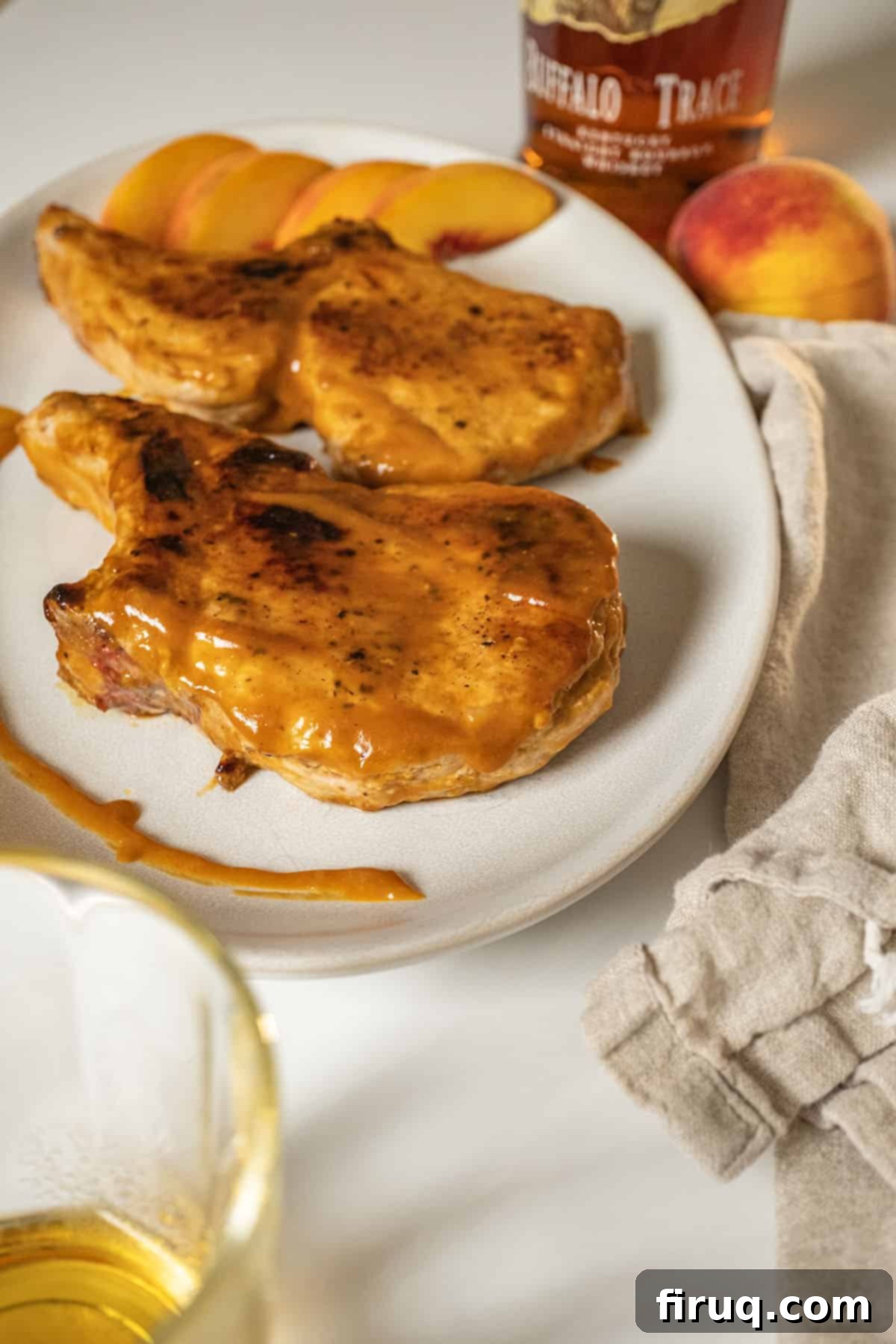 Pork Chops with Bourbon Peach Glaze 10 Bourbon peach glazed pork chops on a plate garnished with peaches and extra sauce.