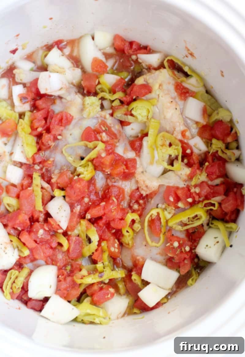 One-Pot Zesty Italian Pepperoncini Chicken 4 Top view down into the slow cooker, showing the raw ingredients for the pulled chicken recipe – chicken thighs, sliced peppers, diced tomatoes, and seasonings – ready for cooking.