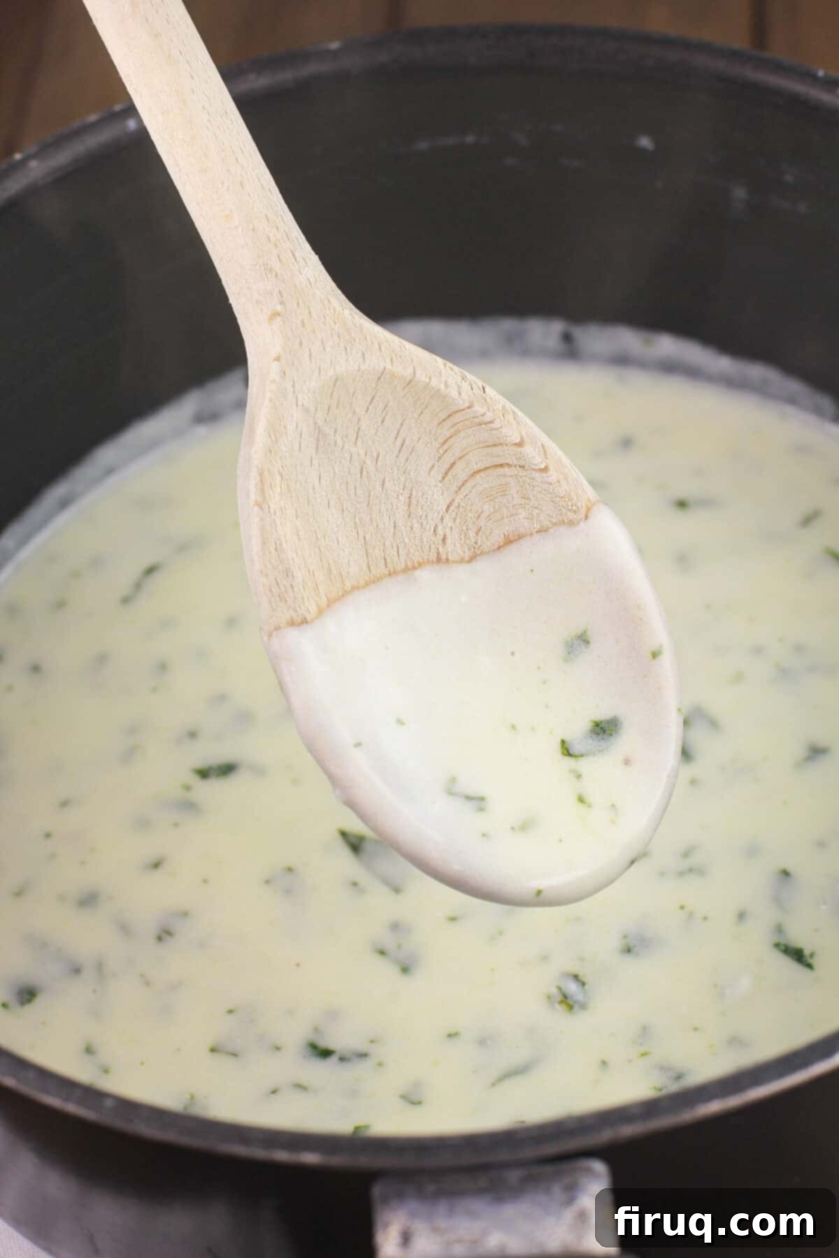 Crab Filled Shrimp with Bacon 8 lemon basil cream on wooden spoon in saucepan, showing its creamy texture