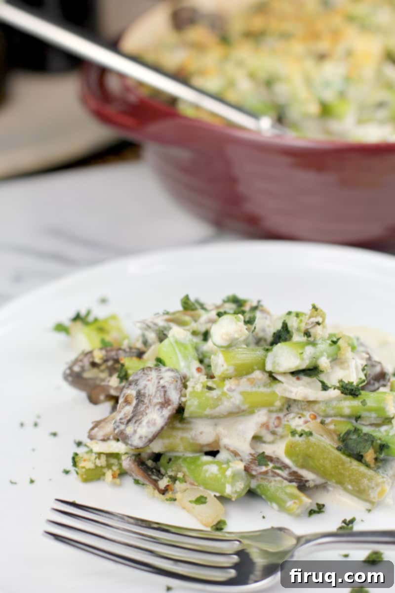 Creamy Asparagus Bake 9 A perfectly portioned serving of Asparagus Casserole on a white plate with a fork, with the full red baking dish in the background.