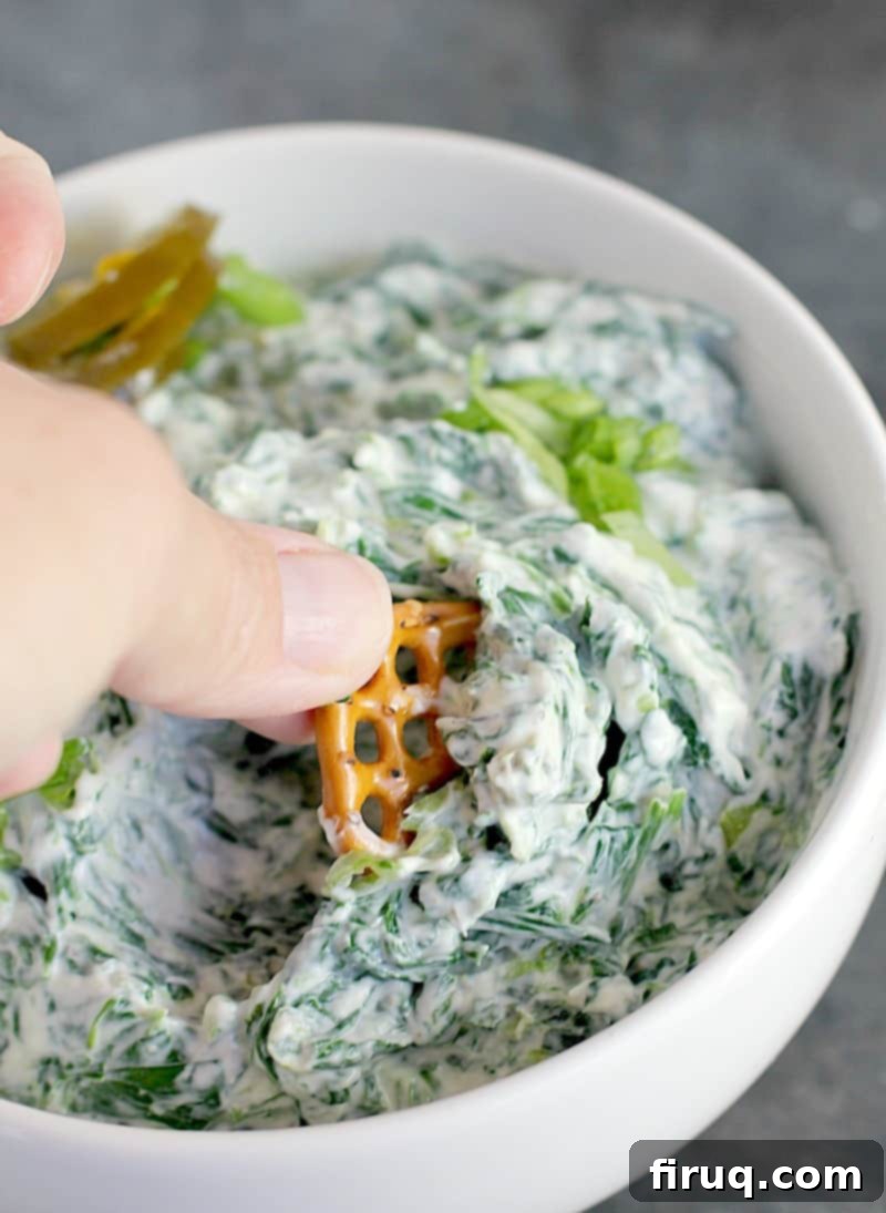 Zesty Slim Spinach Dip 2 hand scooping a pretzel into spinach jalapeno dip