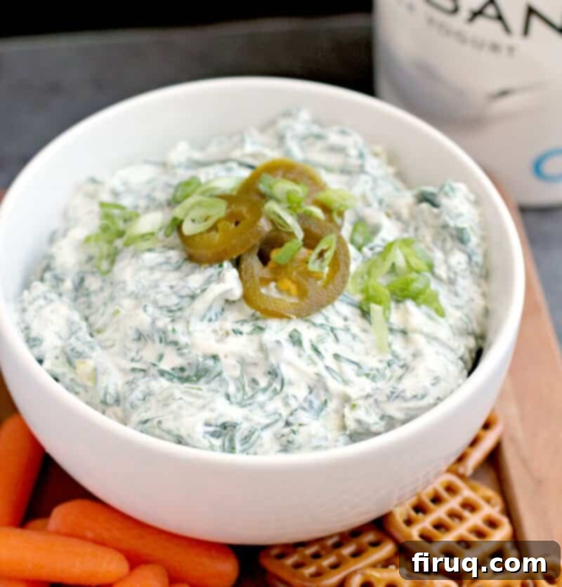 Zesty Slim Spinach Dip 4 dip in a white bowl on a wood platter with baby carrots and square pretzels