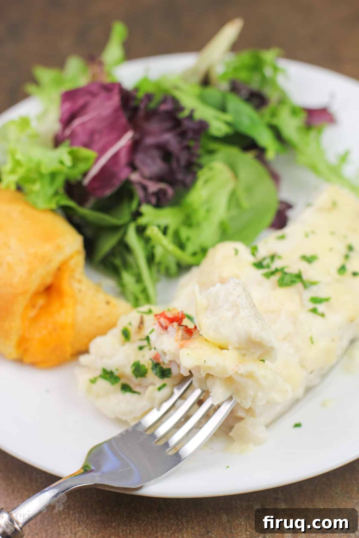 Oven-Baked Haddock, Lobster-Kissed 3 folk holding bite of prepared haddock with lobster sauce on white plate with salad and roll