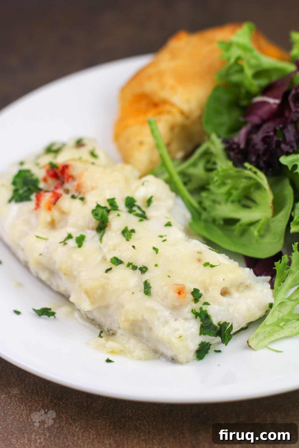 Oven-Baked Haddock, Lobster-Kissed 8 portion of prepared haddock with lobster sauce on white plate with salad and roll