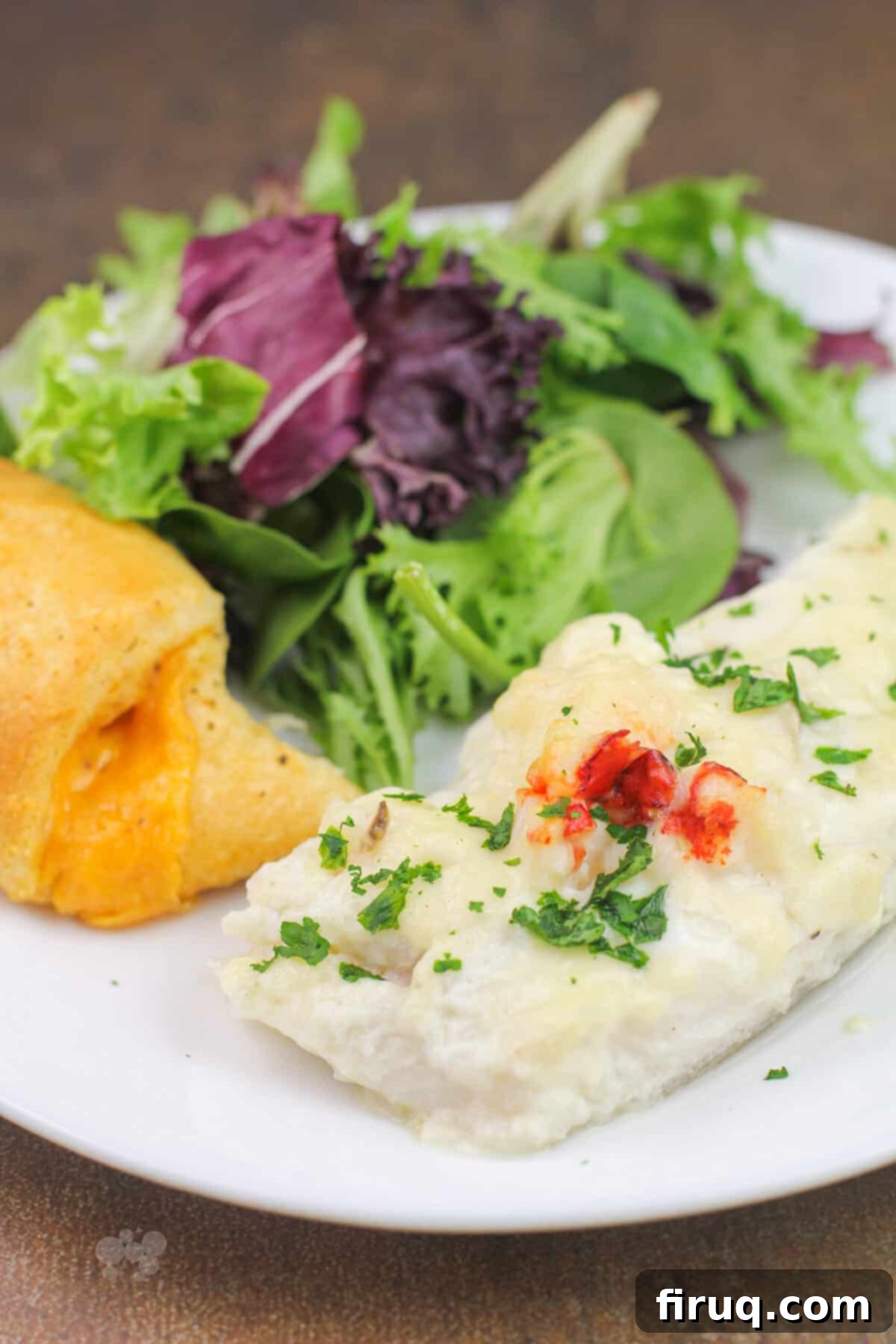 Oven-Baked Haddock, Lobster-Kissed 10 portion of prepared haddock with lobster sauce on white plate with salad and roll