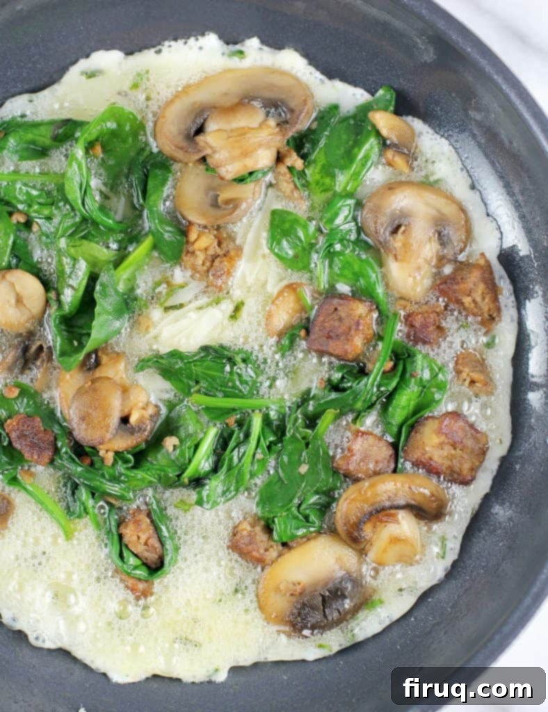 Plant-Powered Omelet with Savory Sausage, Spinach, and Mushrooms 9 skillet with the egg whites cooking, topped with spinach mushrooms and sausage