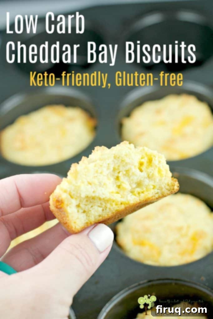 Guilt-Free Cheddar Bay Biscuits 11 Hand holding a low carb cheddar bay biscuit broken in half to show its flaky interior, with additional biscuits in a muffin tin in the background; ideal for pinning and saving