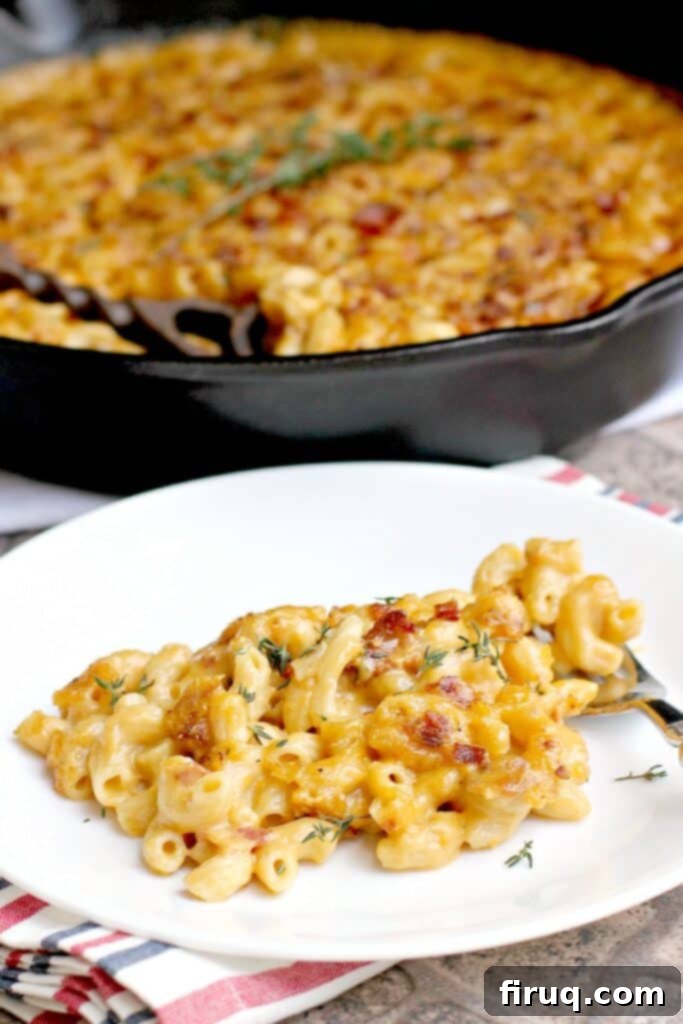Gourmet White Wine Mac and Cheese 5 side view of finished bacon macaroni and cheese plated on a white dish; remainder of the mac n cheese is in the background in a cast iron skillet
