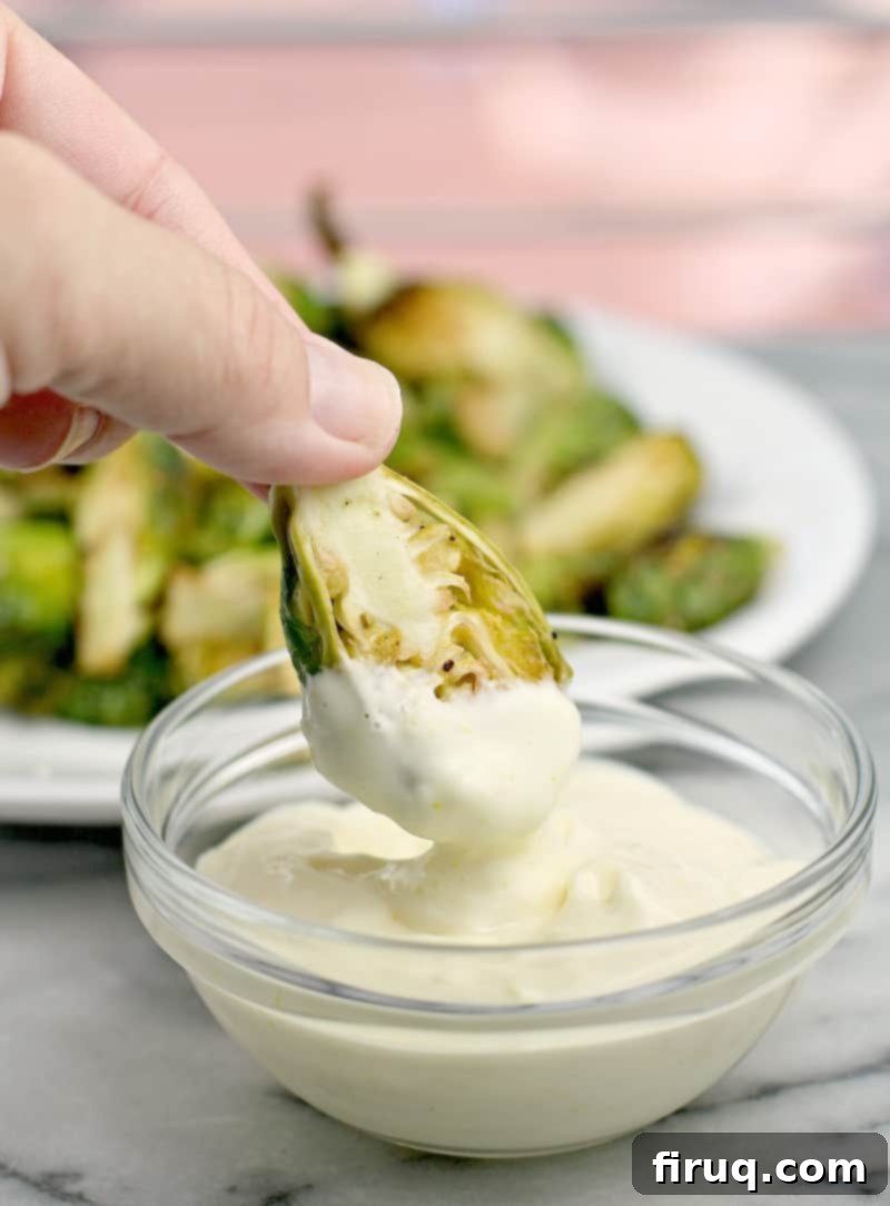 Crispy Air-Fried Brussels Sprouts 2 Hand holding an air-fried Brussels sprout, dipping it into a small glass bowl of bright lemon aioli.