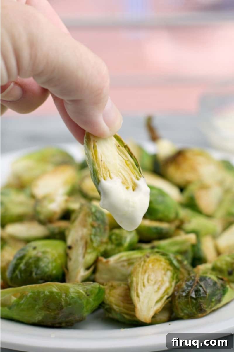 Crispy Air-Fried Brussels Sprouts 7 A hand holding a perfectly air-fried Brussels sprout, generously coated with the creamy and zesty lemon aioli, ready to be enjoyed.