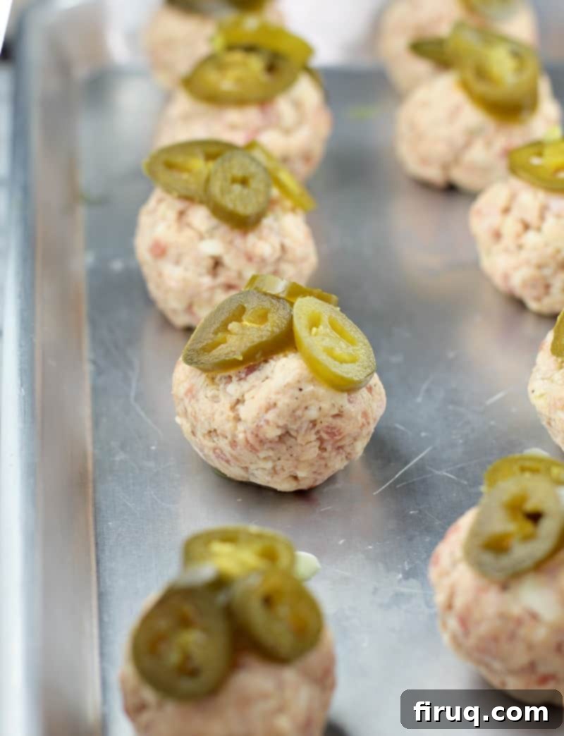 Smoky Sausage Bites 5 uncooked sausage balls on a bake sheet topped with jalapeno