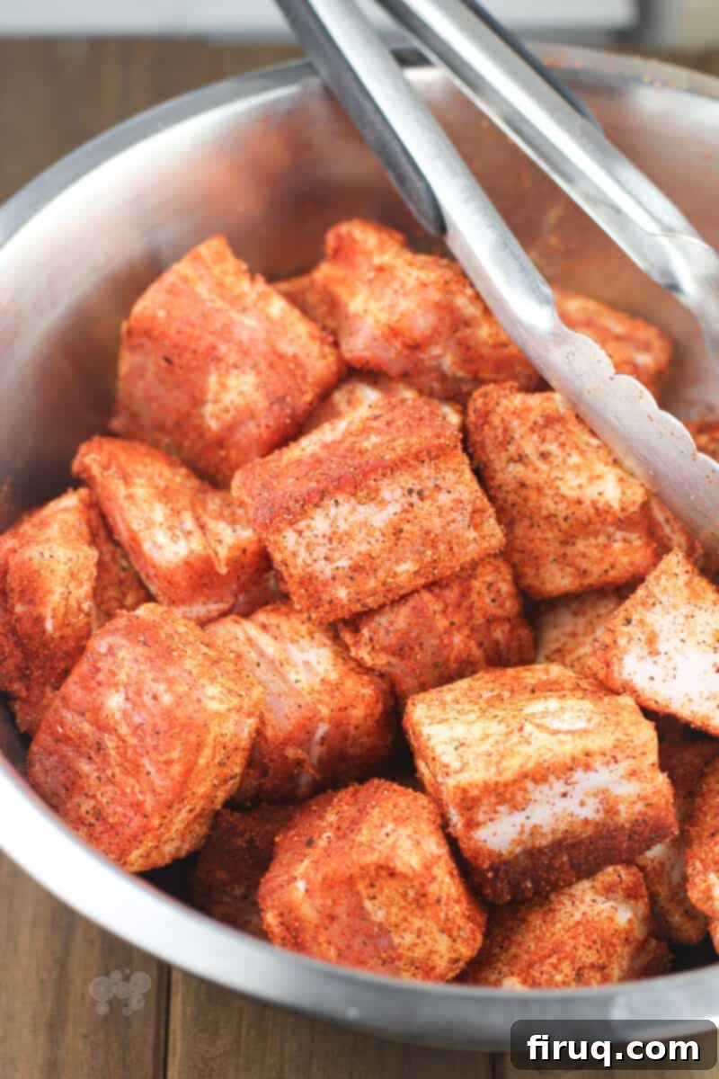 Smoky Glazed Pork Belly Bites 4 Seasoned cubes of pork belly in a metal bowl, ready for smoking, with tongs