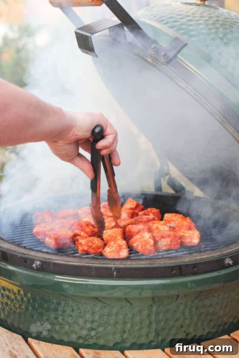 Smoky Glazed Pork Belly Bites 5 Pieces of seasoned pork belly being placed onto the grill grate inside a Big Green Egg smoker