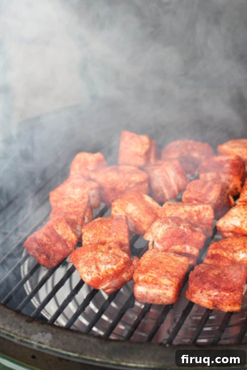 Smoky Glazed Pork Belly Bites 10 Uncooked, seasoned pork belly cubes on a smoker grill grate, ready for smoking