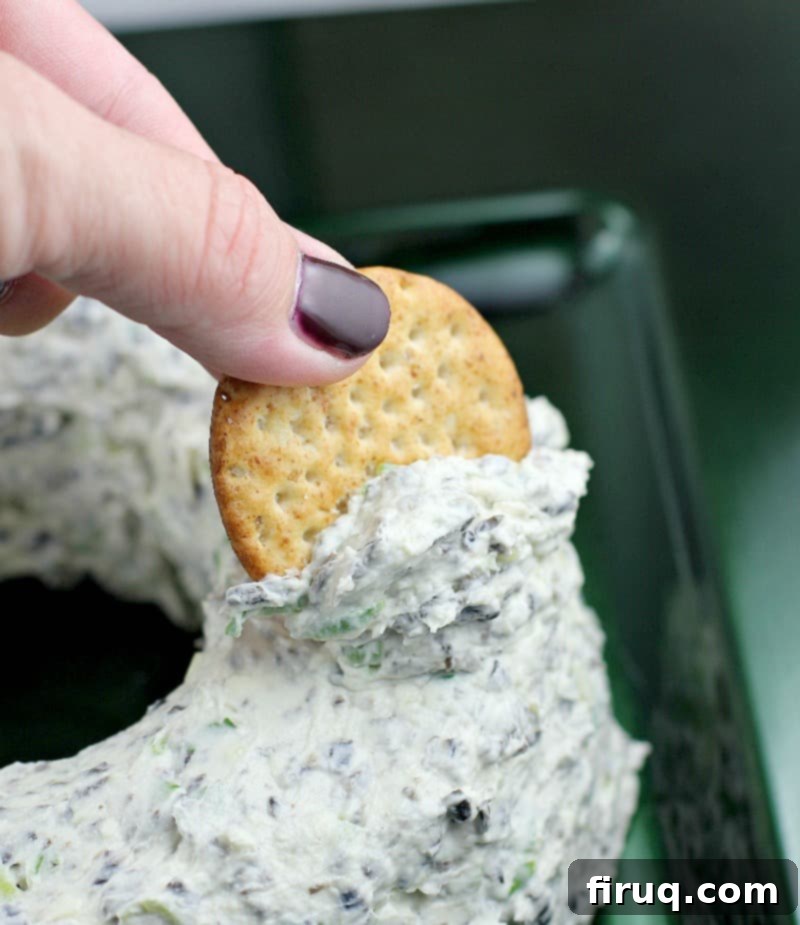 Festive Olive & Scallion Wreath Dip 15 A side view of a hand scooping a generous portion of the creamy Scallion Olive Party Dip from the side of the festive cheese wreath.
