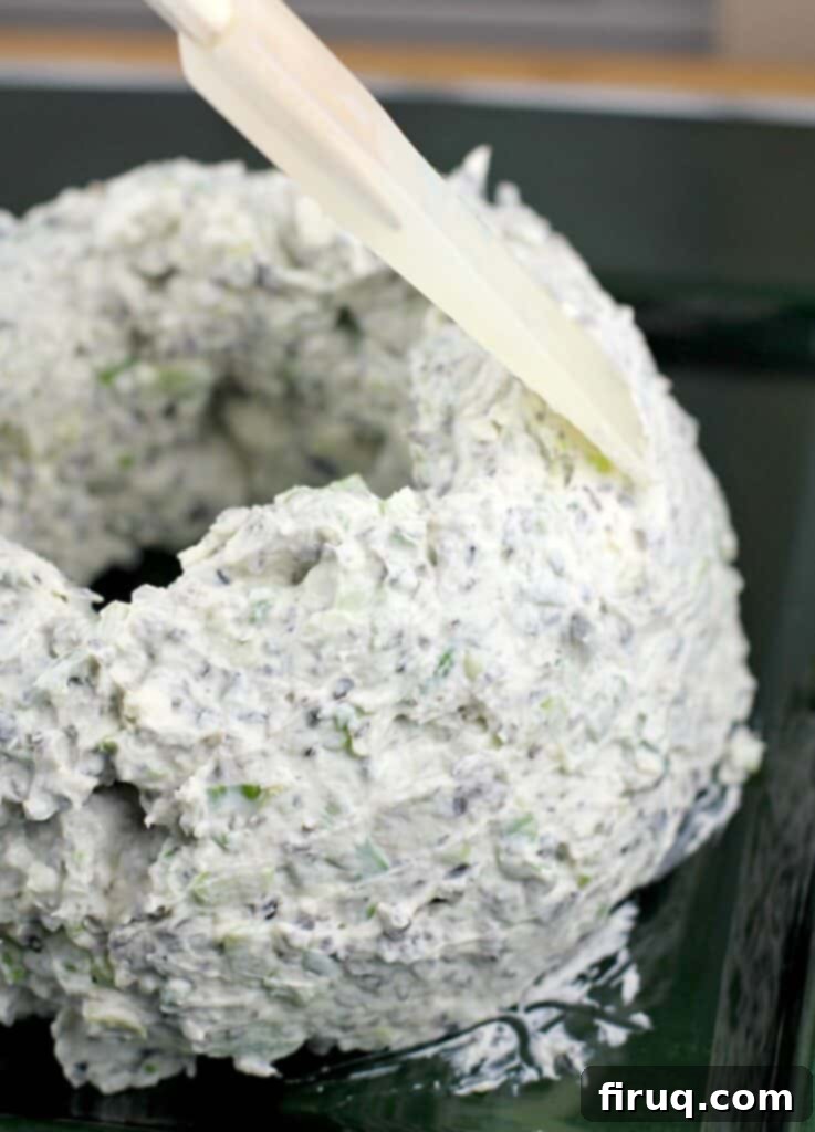 Festive Olive & Scallion Wreath Dip 8 A rubber spatula carefully smoothing the surface of the Scallion Olive Party Dip cheese wreath, perfecting its circular shape.
