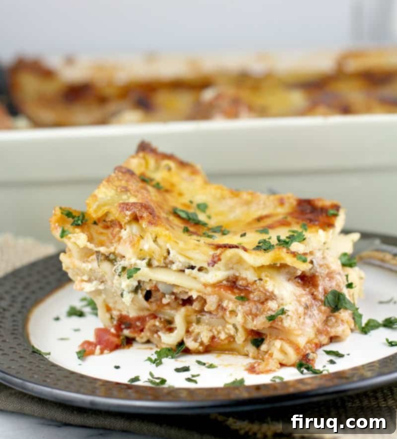 Classic Lasagna 2 side view of a large square of lasagna plated on a white plate with brown rim, lasagna bake dish is in the back ground