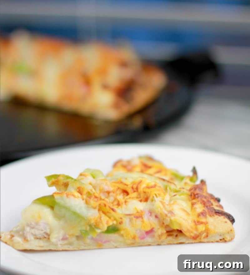 Spicy Buffalo Turkey Pizza 4 Side view of a slice of pizza on a white plate (green bell pepper, turkey, and onion toppings are peeking out from the cheese); finished pizza is in the background on a black pizza stone