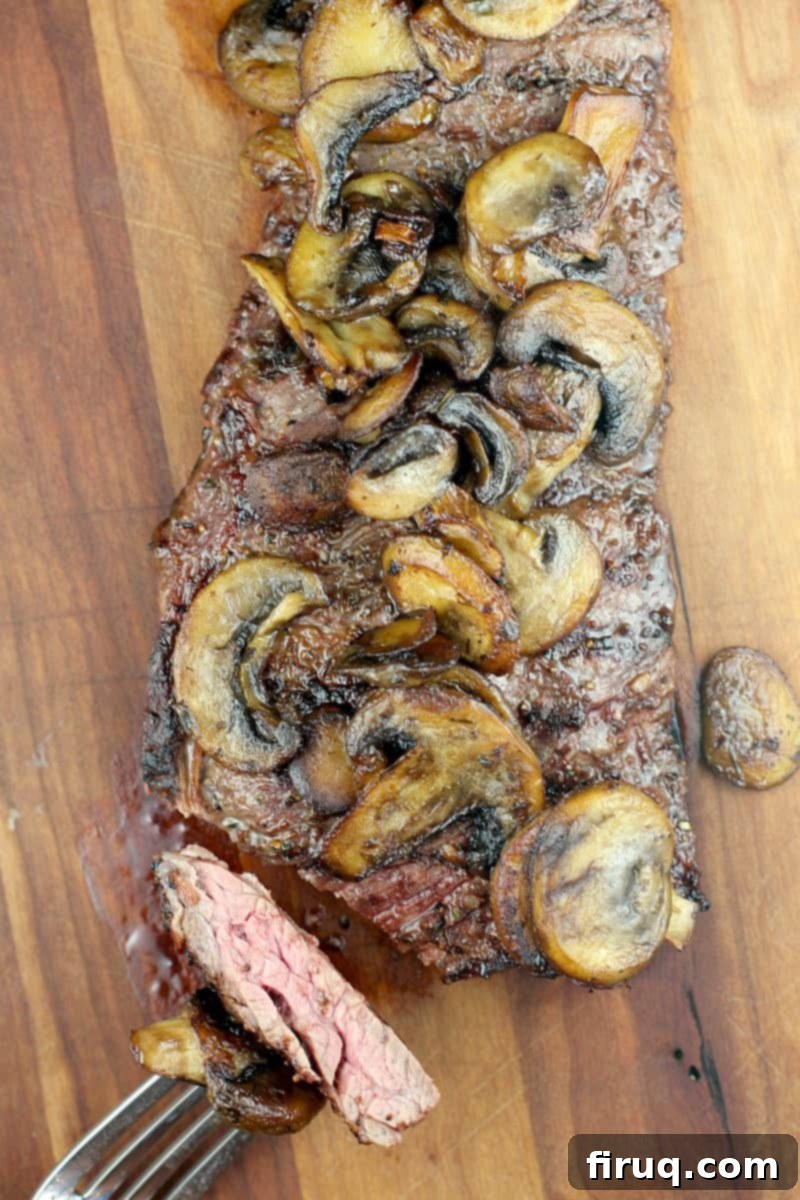 Bistro Garlic Butter Skirt Steak with Sautéed Mushrooms 7 top down view of cooked steak on wood board with fork holding cut piece