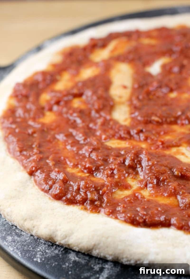 Perfect Homemade Pizza Sauce 2 uncooked pizza dough with sauce spread on, on a black pizza stone