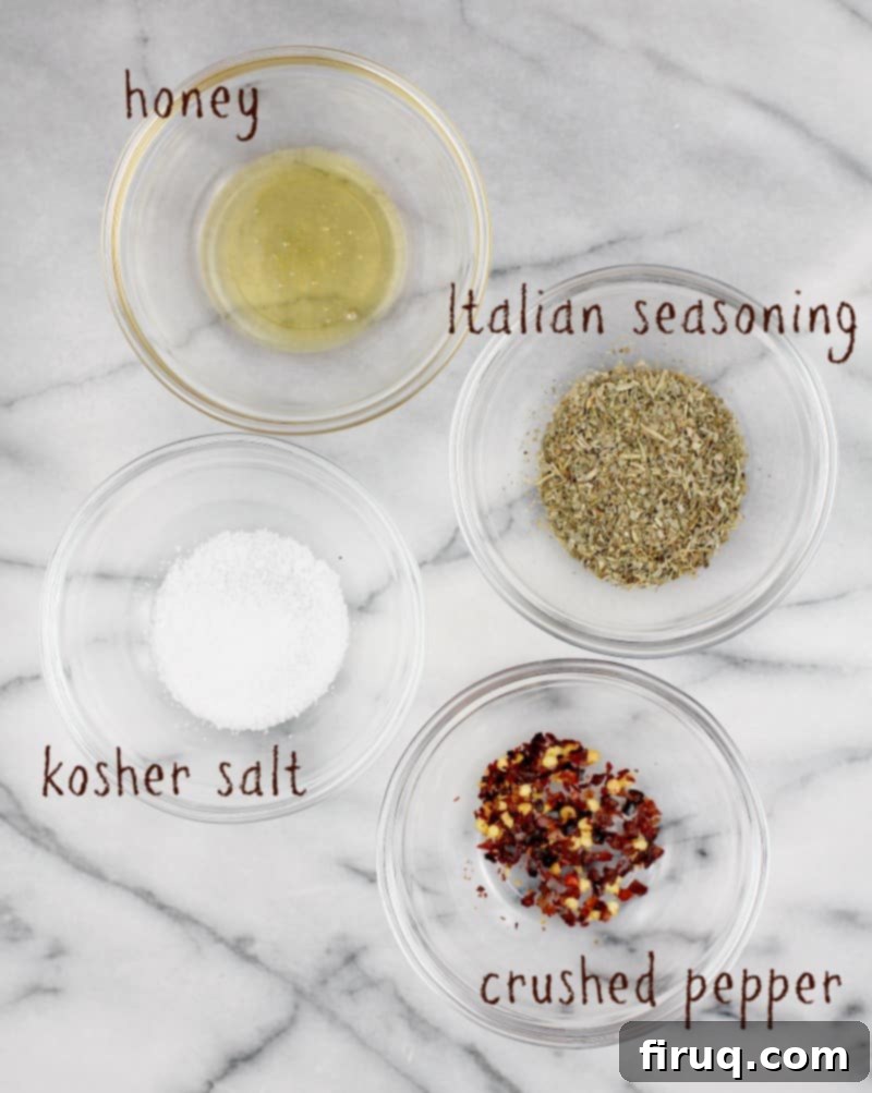 Perfect Homemade Pizza Sauce 5 marble board on which are 4 small glass bowls showing ingredients: honey, italian seasoning, salt, and crushed red pepper