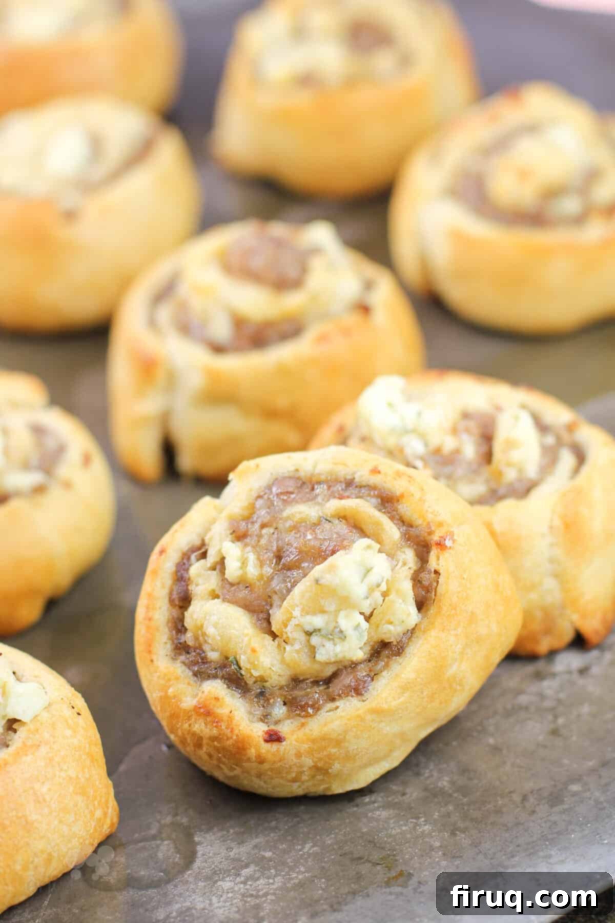 Creamy Boursin Sausage Swirls 3 Freshly baked sausage and Boursin pinwheels on a baking sheet, with one turned on its side to reveal the delicious layers.